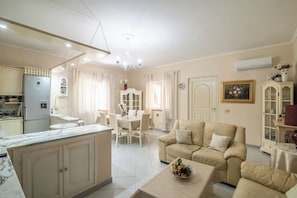 A living room with a beige sofa, a dining table, and a kitchen area with a refrigerator. - San Nikola House (Olbia)