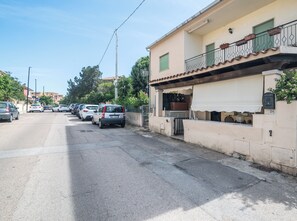 A street view with parked cars, a building with a balcony, and a clear sky. - San Nikola House (Olbia)