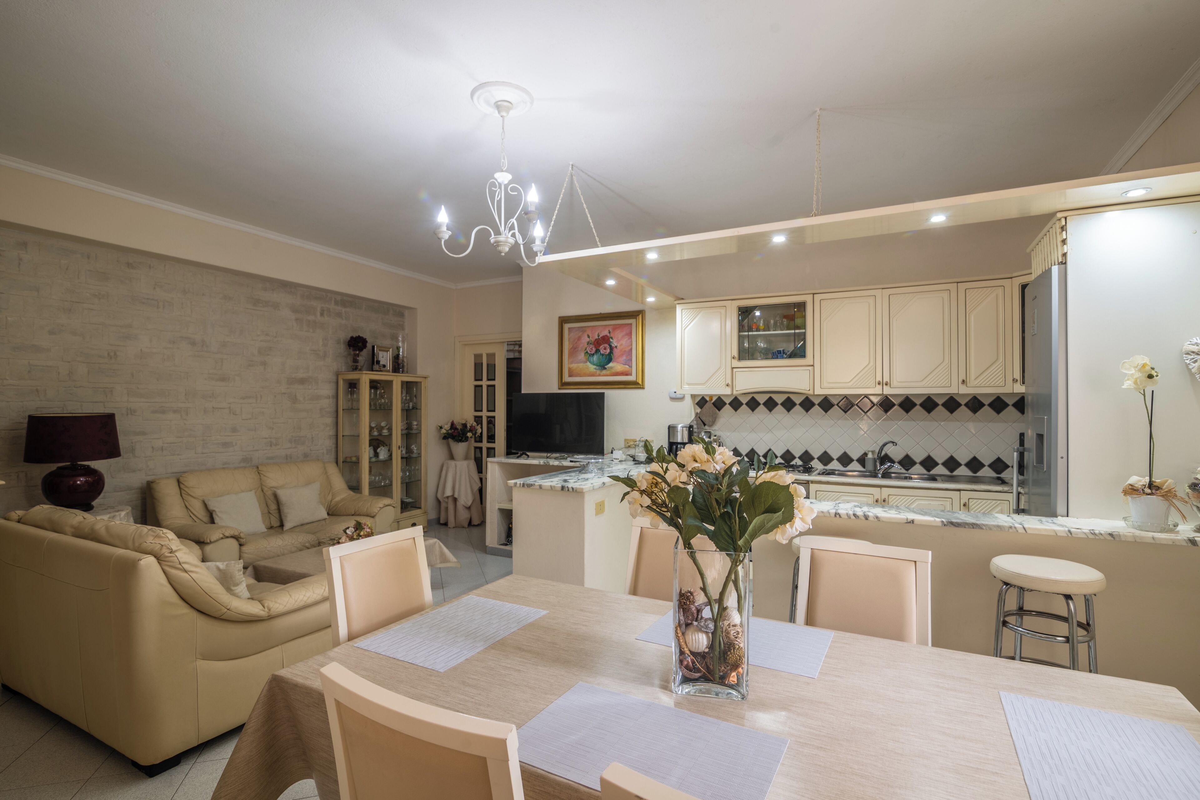 A modern kitchen with a dining area, a chandelier, and a vase with flowers on the table.