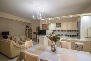 A modern kitchen with a dining area, a chandelier, and a vase with flowers on the table. - San Nikola House (Olbia)