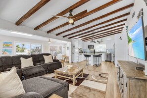 A spacious living area with a sofa, coffee table, and a kitchen in the background. - HOLIDAY SHORES BEACH COTTAGE! WATERFRONT! DOCK! WALK TO BEACH! PET FRIENDLY!!! (Fort Myers Beach)