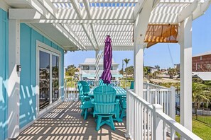 A covered outdoor area with a table and chairs, a purple umbrella, and a view of a house and palm trees. - HOLIDAY SHORES BEACH COTTAGE! WATERFRONT! DOCK! WALK TO BEACH! PET FRIENDLY!!! (Fort Myers Beach)