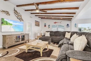 Ein Wohnzimmer mit Ecksofa, Flachbildfernseher, Holzbalken und dekorativer Wandgestaltung.