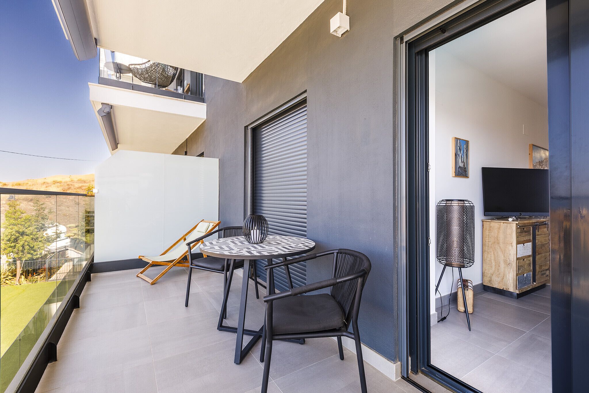 Un balcon avec une table et des chaises, un téléviseur et un meuble.