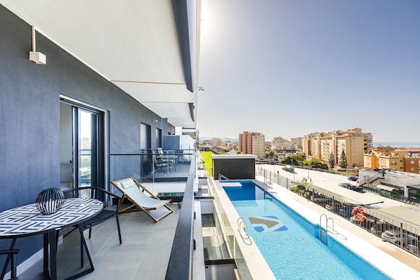Una piscina al terrat amb vista a la ciutat, una taula amb cadires i una barana de vidre.