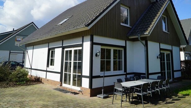 A two-story house with a tiled roof, large windows, and a patio with a table and chairs. - Daelenbroeck Sauna 16 (Susteren)