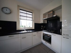 Een moderne keuken met witte kasten, een zwart aanrecht, een roestvrijstalen spoelbak, een raam met zonwering, een klok en een fornuis.