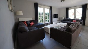 A modern living room with a sofa set, a coffee table, a TV, and large windows. - Daelenbroeck Sauna 16 (Susteren)
