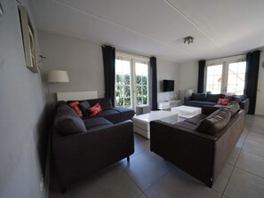 Een moderne woonkamer met een zithoek, een salontafel, een televisie en grote ramen.