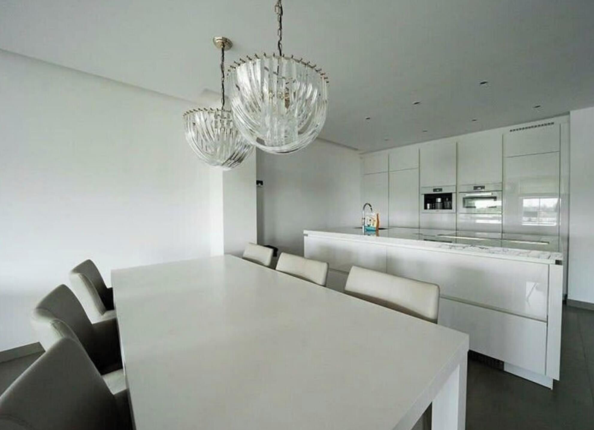 A modern kitchen with white cabinetry, a central island, and a dining area with a white table and chairs.
