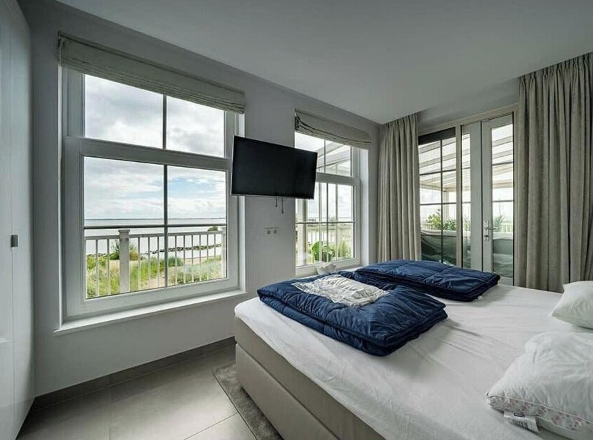 A hotel room with a bed, a TV, and large windows with a view.