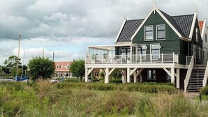 A green house with a balcony and a staircase leading to the entrance. - Zuiderzee Luxe 6 (Uitdam)
