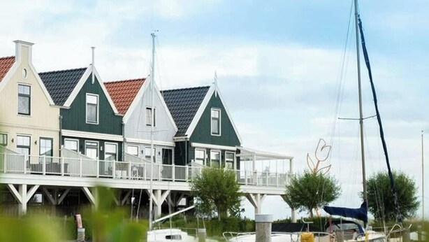 A waterfront property with a dock, a sailboat, and a row of houses with a balcony. - Zuiderzee Luxe 6 (Uitdam)