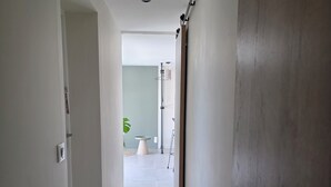 Un pasillo con puerta de madera, pared blanca y suelo de baldosas.