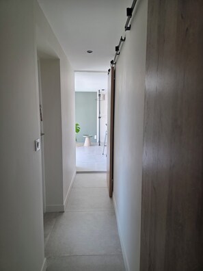 Ein Korridor mit einer Holztür, einer weißen Wand und einem gefliesten Boden.