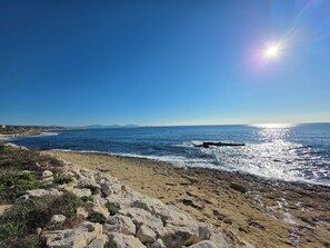 Ein felsiger Strand mit Wellen, einem klaren Himmel und fernen Bergen.