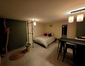 Ein Schlafzimmer mit einem Bett, einem Schreibtisch, einem Stuhl, einer Pendelleuchte, einer Stehlampe und einem kleinen runden Tisch.