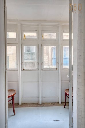 Ein Zimmer mit weißen Wänden, Holzboden und einem großen Fenster. Es gibt zwei Stühle und eine Tür mit Fenster.