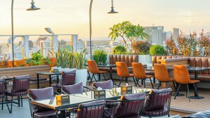 A rooftop bar with tables and chairs, a view of the city skyline, and potted plants. - Le Blend Residence  (Ou Chrov)