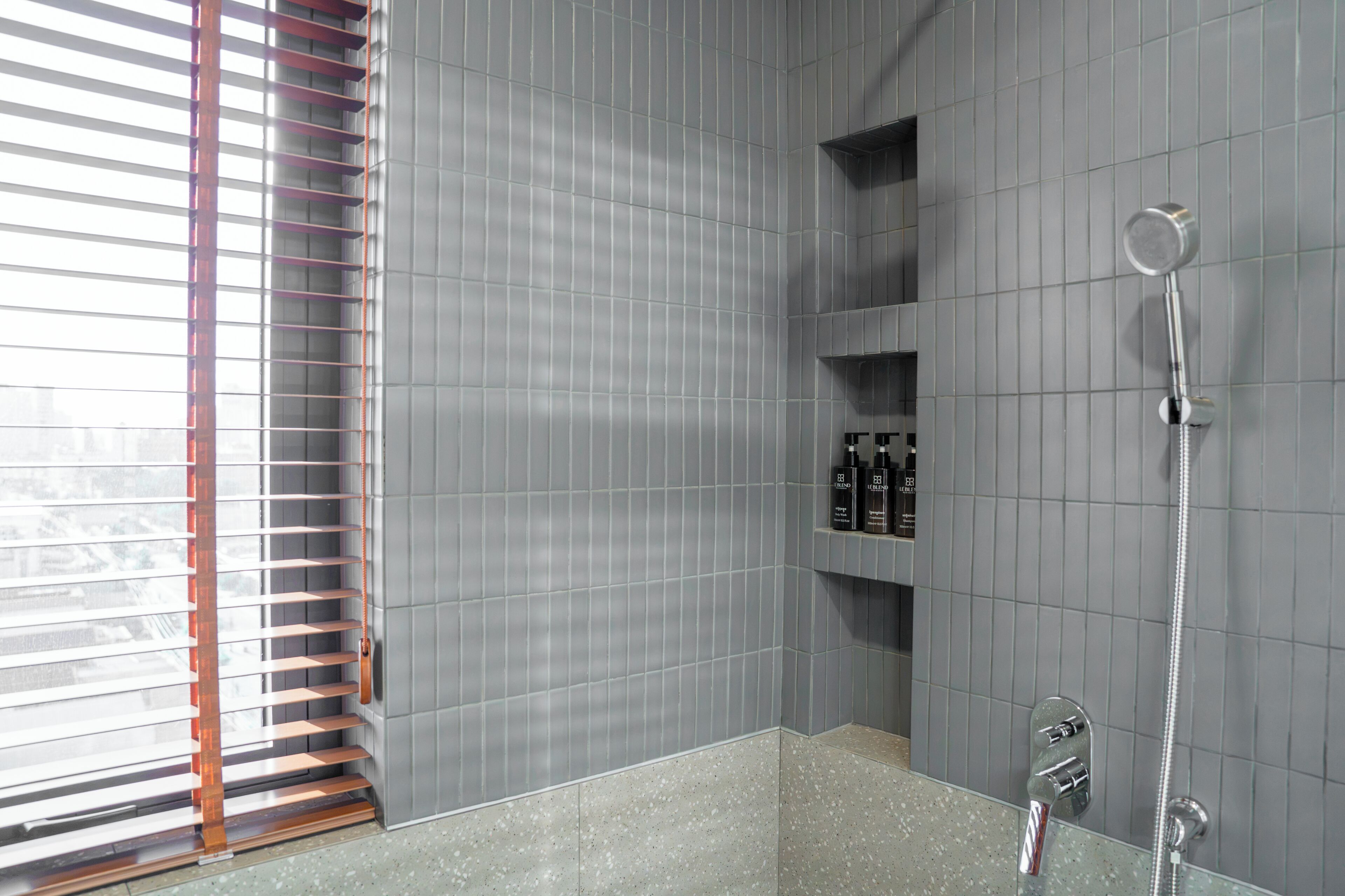 A modern bathroom with a large bathtub, a shower, and a window with blinds.