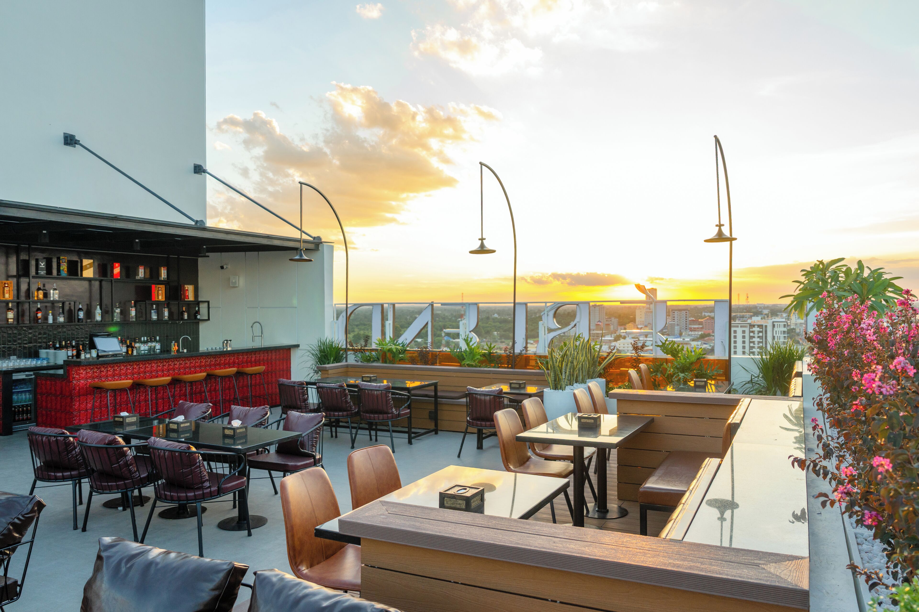 A rooftop bar with seating and a city view at sunset.