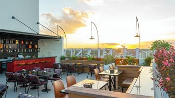 A rooftop bar with seating and a city view at sunset.