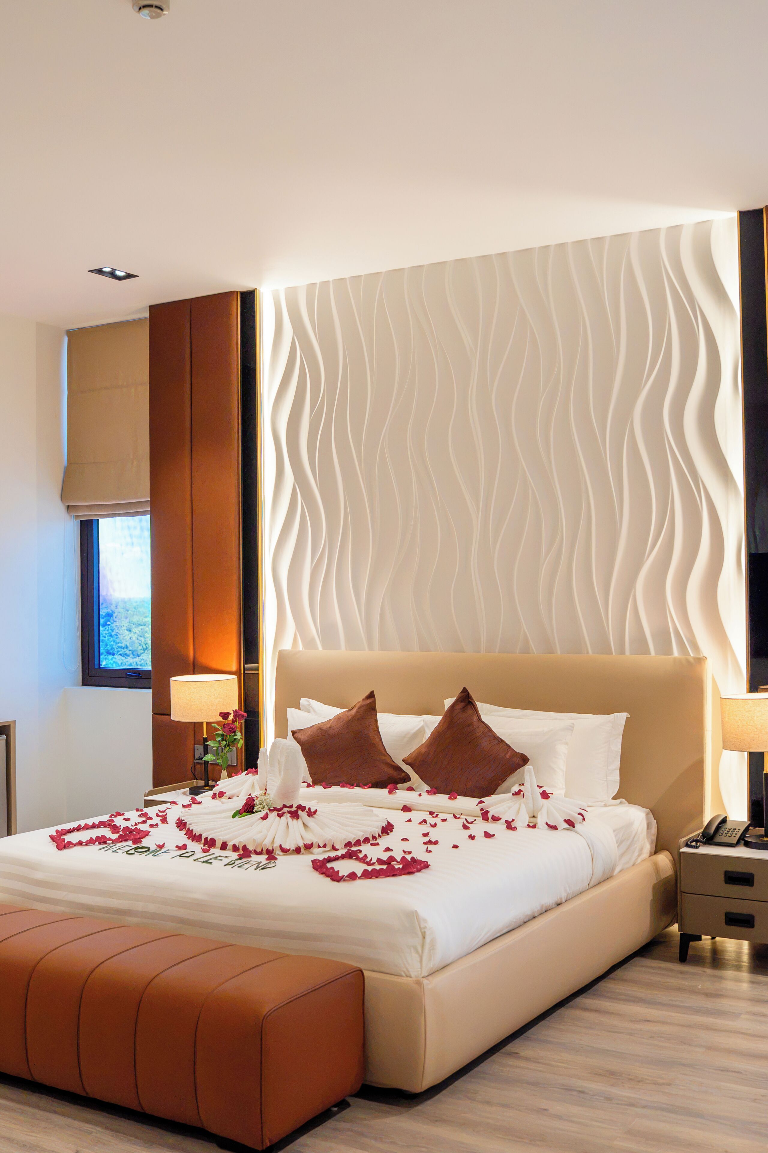 A hotel room with a bed, a nightstand, a lamp, a window, and a wall with a wavy pattern.