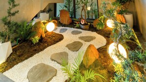 A multi-level indoor space with a modern architectural design, featuring a central garden area with rocks, plants, and lighting. - Le Blend Residence  (Ou Chrov)