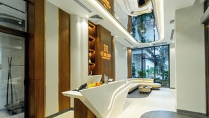 A modern reception desk with a wooden accent, a glass partition, and a seating area with a view of greenery. - Le Blend Residence  (Ou Chrov)