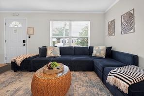 A living room with a dark blue sectional sofa, a woven coffee table, and a striped throw blanket. - 3BR Private Pool Home Near Indian Rocks Beach & Clearwater Pets + Fenced Yard (Largo)