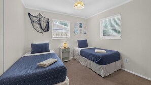 Une chambre avec deux lits, une table de chevet, un luminaire fixé au mur et une fenêtre avec des stores.