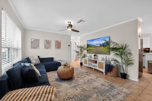 A living room with a dark blue sofa, a large flat-screen TV, a ceiling fan, and a large window with blinds. - Private pool near 8 minutes to Indian Rocks Beach (Largo)