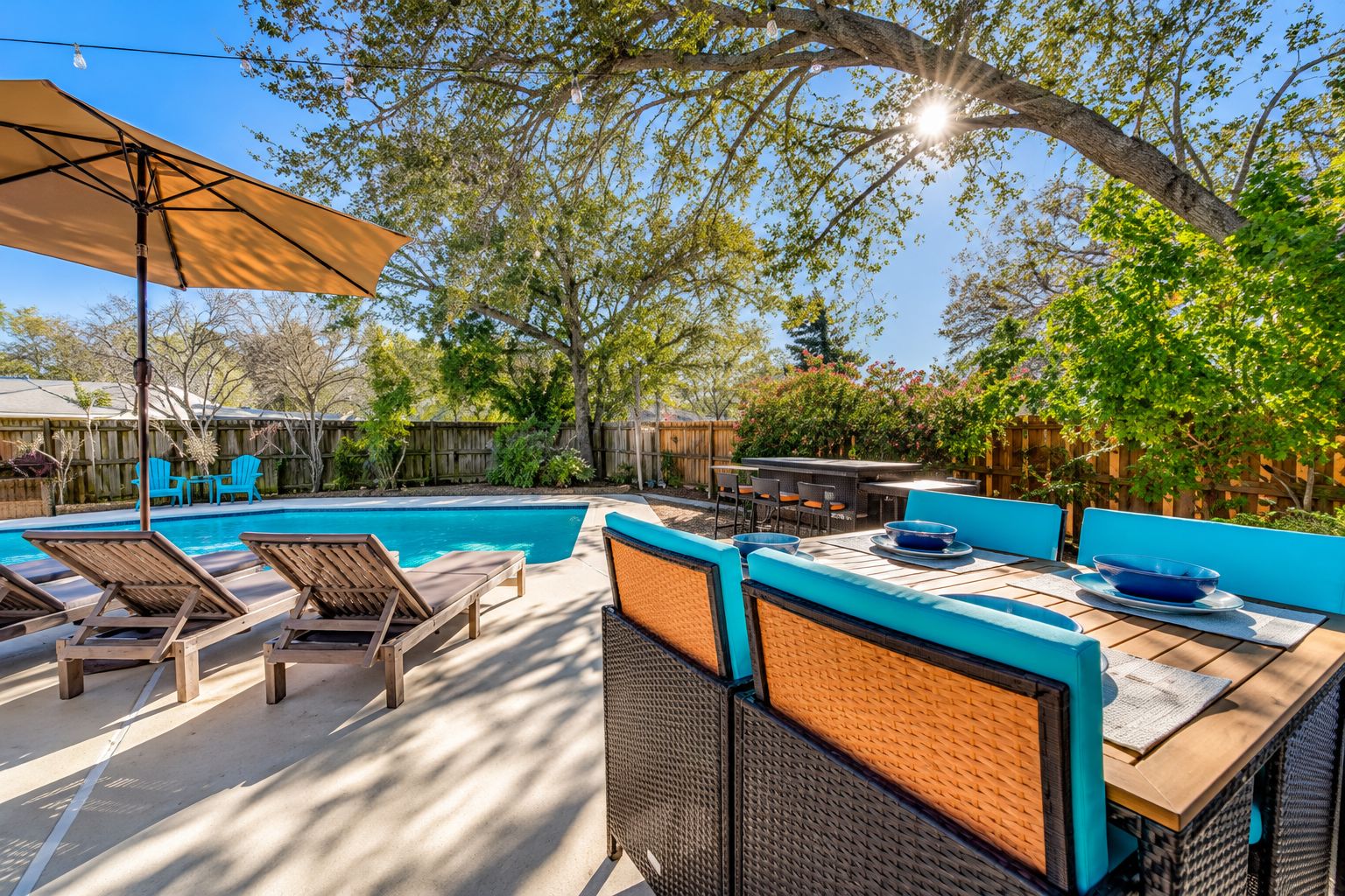 A backyard with a swimming pool, lounge chairs, a barbecue area, and a dining table.