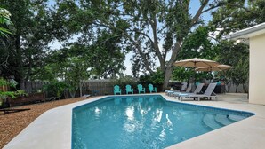 Une piscine rectangulaire dotée d’une plage de couleur claire, entourée d’arbres et d’une clôture en bois.