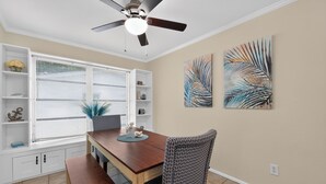 Un espace repas comprenant une table en bois, des chaises à motifs, un ventilateur de plafond et des œuvres d’art murales.