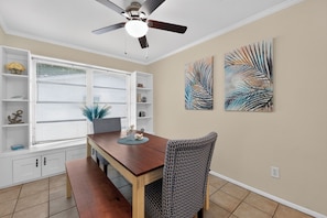 A dining area with a wooden table, patterned chairs, a ceiling fan, and wall art. - 3BR Private Pool Home Near Indian Rocks Beach & Clearwater Pets + Fenced Yard (Largo)