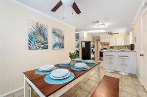 A dining area with a wooden table set for four, two ceiling fans, and a kitchen in the background. - Private pool near 8 minutes to Indian Rocks Beach (Largo)