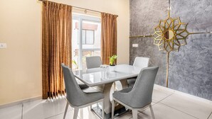 Een eetgedeelte met een glazen tafel, grijze stoelen en een decoratief wandobject.