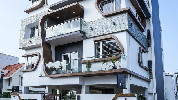 Een modern meerlaags gebouw met balkons, een glazen dak en een bord waarop 'BLISS' staat.