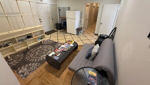 Een moderne woonkamer met een bank, salontafel en een kamerbreed tapijt. Er is een keuken met een koelkast en een eettafelstoel.