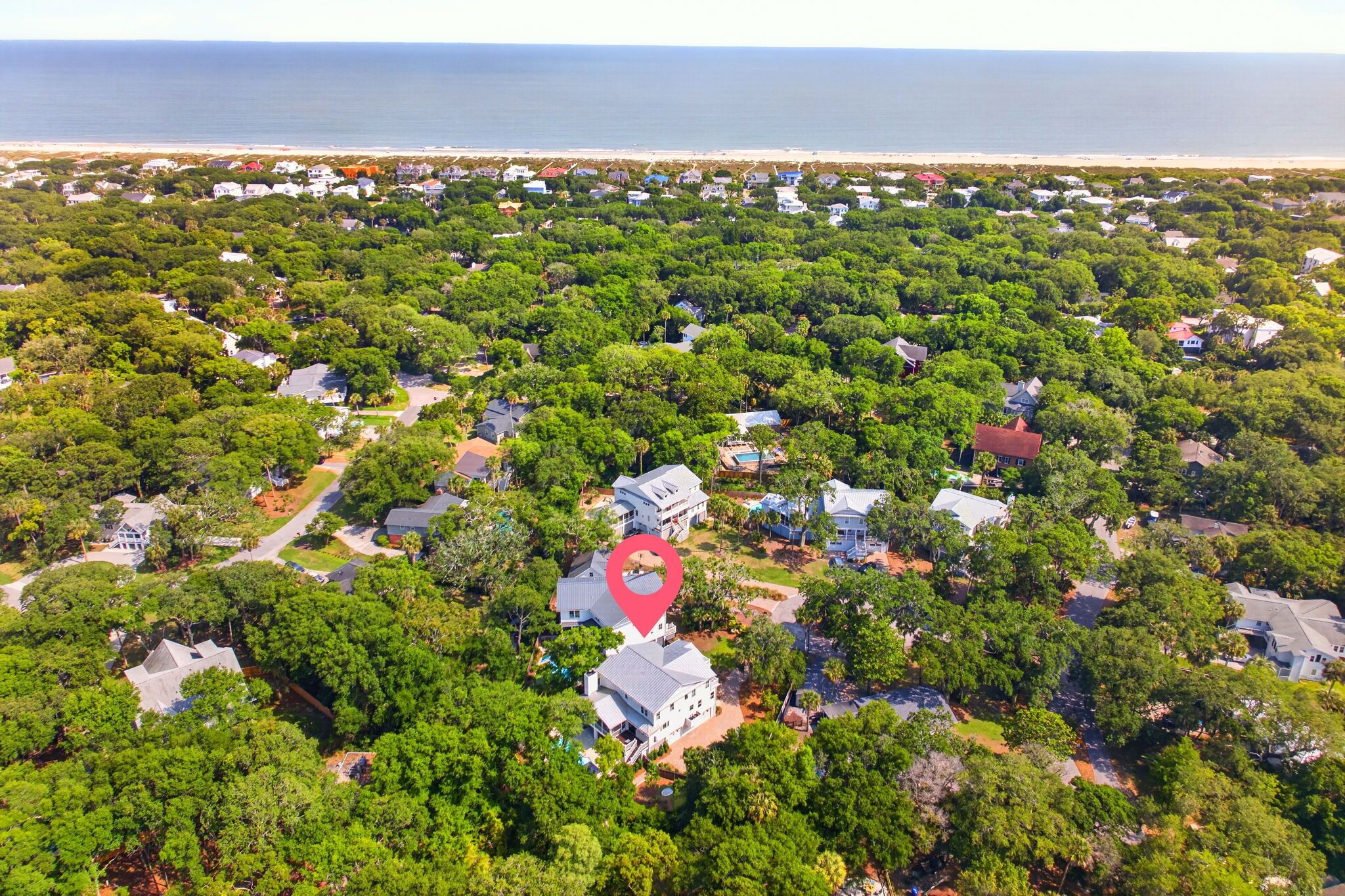 Luchtbeeld van een woongebied met huizen, omgeven door weelderige begroeiing, een strand in de verte en een rode markering voor de locatie.