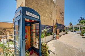 A traditional telephone booth with a wooden interior, located in a courtyard with plants and a pool area. - Gozo Couple Bungalow No 2 · Pool, Cabana, BBQ Deck (Gozo)