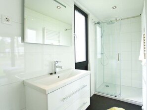 A modern bathroom with a white vanity, a glass shower enclosure, and a large mirror. - Cube Maximaal 6 (Breskens)