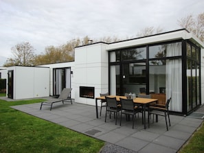 A modern outdoor patio with a dining table and chairs, a fireplace, and a glass-enclosed structure. - Cube Maximaal 6 (Breskens)