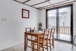 Uma área de refeições com mesa e cadeiras de madeira, um vaso com planta e uma porta de vidro deslizante que dá para uma varanda.