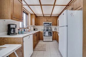 Eine kleine Küche mit Holzausstattung, einer Kaffeemaschine, einer Mikrowelle, einem Backofen und einem Kühlschrank.