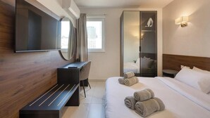 Habitación de hotel con cama, escritorio, silla, televisor, armario y ventana.