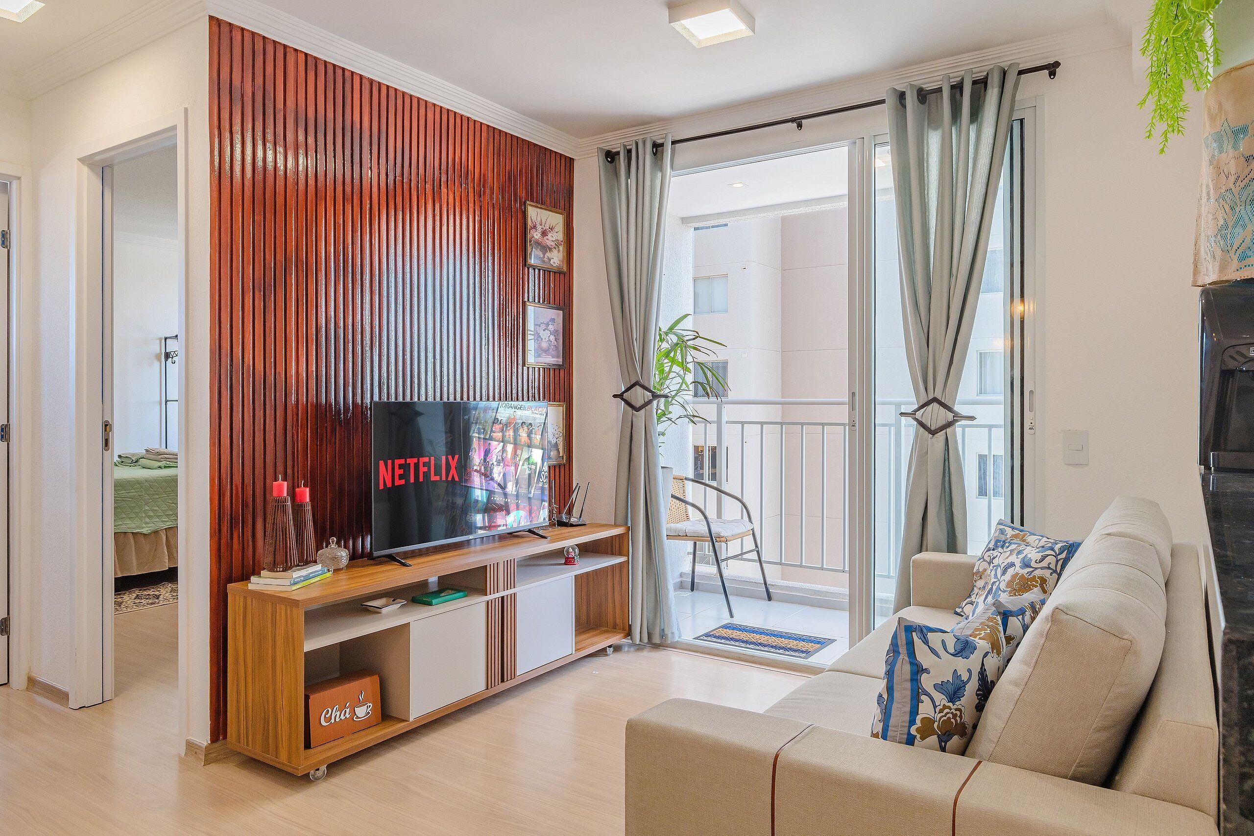Ein Wohnzimmer mit Fernseher, Holzwand, Sofa und einem Balkon mit Blick.
