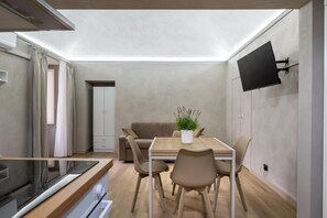 Ein kompakter Wohnbereich mit Küchenzeile, Essbereich, Sofa und einem an der Wand befestigten Flachbildfernseher.