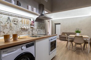 A compact kitchen with a washing machine, a stove, a sink, and a dining area with chairs and a table.